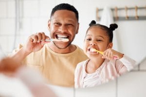 Father and daughter brushing bright white teeth together