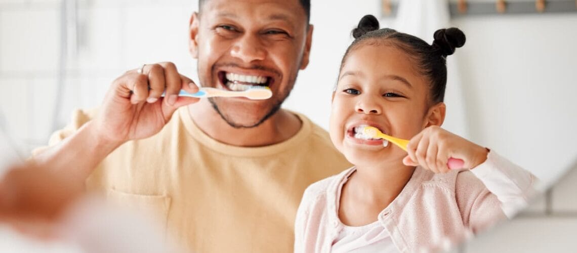 Father and daughter brushing bright white teeth together